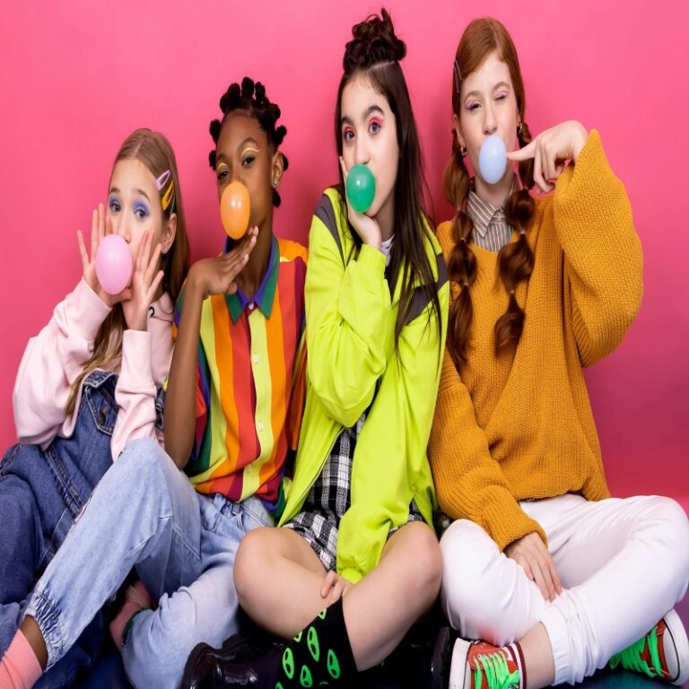 Group of four diverse preteen girls sitting cross-legged on the floor, blowing large colorful bubble gum bubbles, wearing vibrant rainbow and neon outfits against a bright pink background, joyful and playful expression"