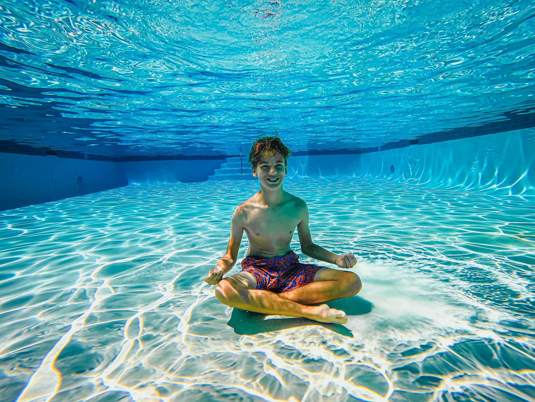 topless boy sitting underwater in a swimming pool